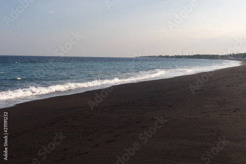 Clean and empty beach of black volcanic sand on the coast of Bali