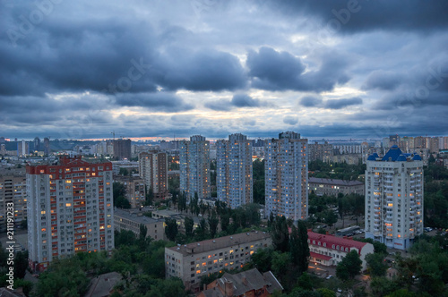 Beautiful night cityscape with cloudy sky/Aerial view of Kyiv's city residential district after the sun has set.Dark rainy clouds in the blue sky over the city.Urban night cityscape