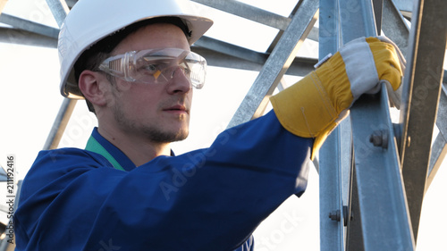 The builder or engineer, in a blue robe, in a white helmet, check the technical review for strength, prepare to install electric poles, an electric tower, energy, workers.