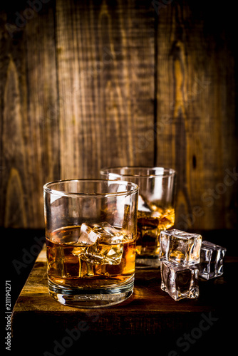 Canvas Print Two whiskey shot glasses on dark wooden background, with ice cubes, copy space