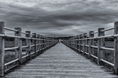 Black and white of a couple walking away on a pier as a storm is rolling in