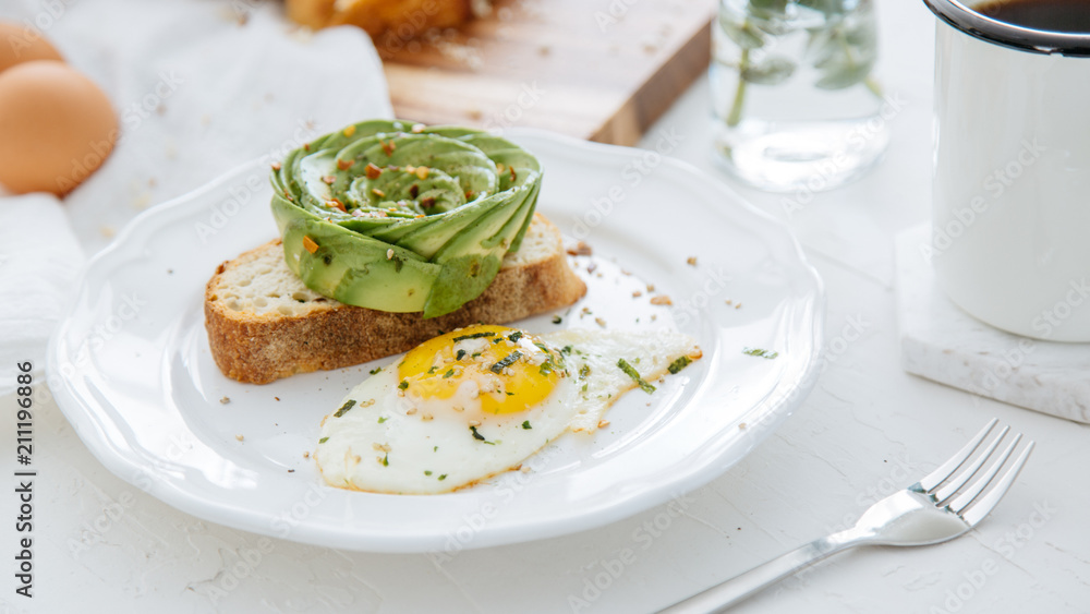 Breakfast setting featuring avocado rose on toast, sunny side up egg and coffee.