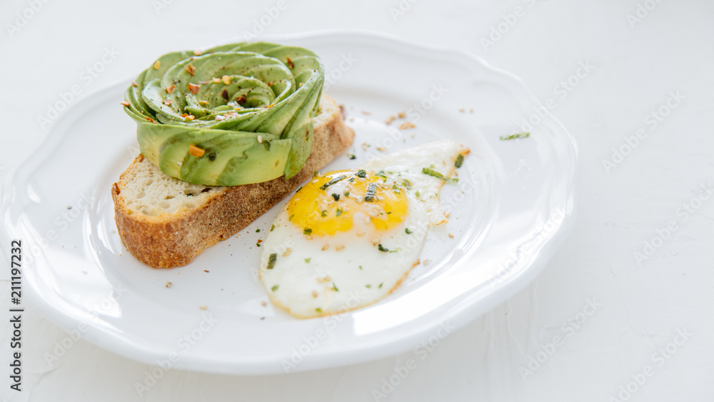 Avocado rose on toast with sunny side up egg on white plate and white background.