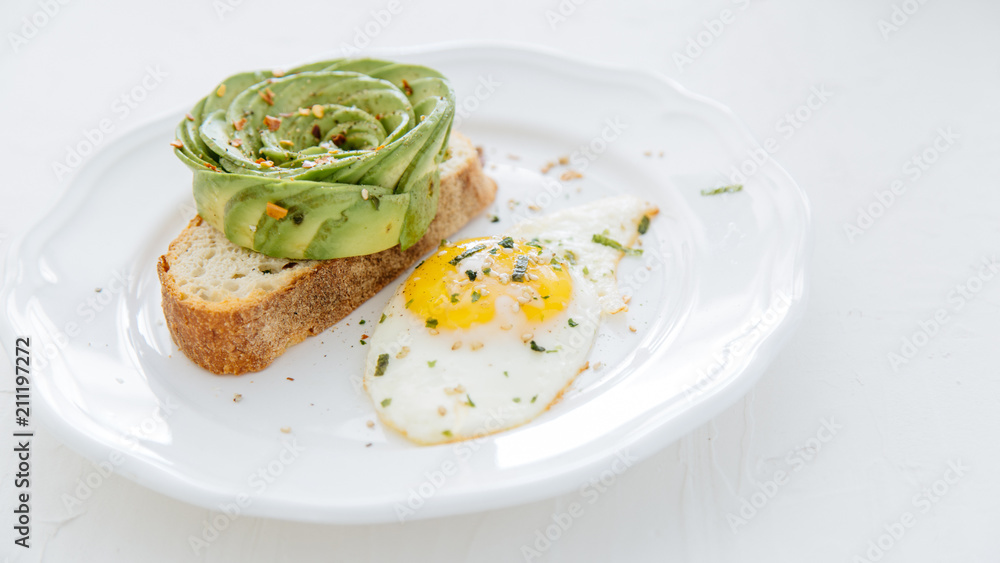Avocado rose on toast with sunny side up egg on white plate and white background.