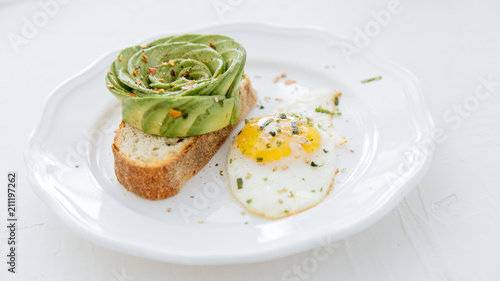 Avocado rose on toast with sunny side up egg on white plate and white background.