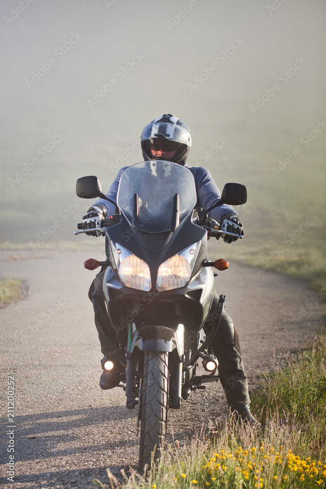 Obraz premium man riding a motorbike on foggy road in early morning
