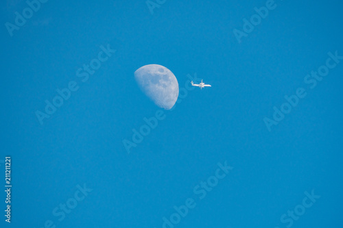 a white plane fly away from the half moon under the blue sky photo