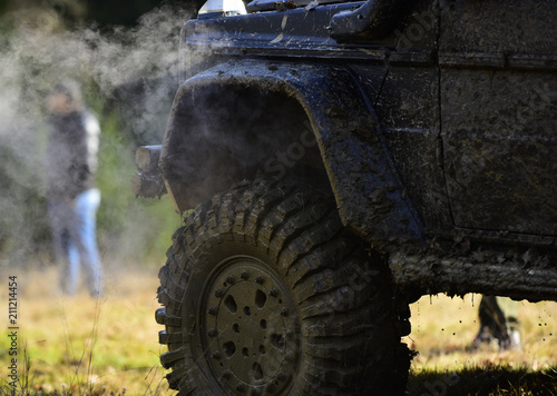 Part of vehicle covered with mud and man near it. SUV on nature background, close up. Side of car covered with dirt and cloud of smoke Off road racing, force and extreme entertainment concept