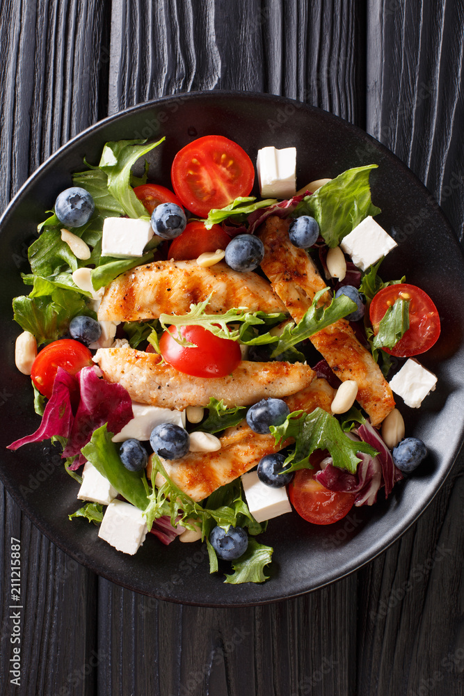Low-calorie salad with blueberries, feta, chicken, nuts, tomatoes and lettuce close-up. Vertical top view