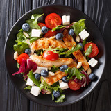 Fresh grilled chicken salad with blueberries, cheese, nuts, tomatoes and lettuce close-up. top view