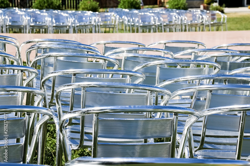 Rows of empty metal chair seats installed for some business event or performance,festival.Many empty parallel arranged silver chairs.conference chair prepare to use. © Yulia