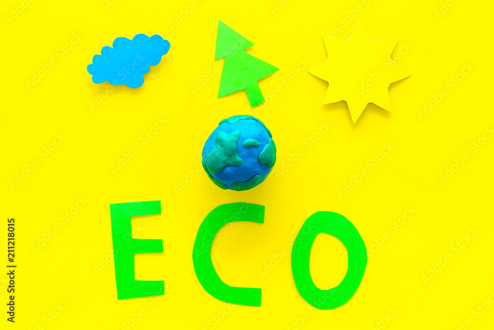 Eco icon cutout near plastiline symbol of planet Earth and environment as sun, trees, clouds on yellow background top view Eco icon cutout near plastiline symbol of planet Earth and environment as sun, trees, clouds on yellow background top view