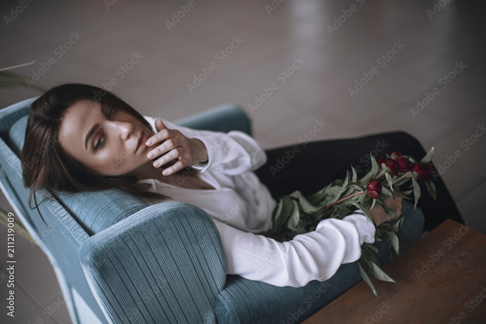 Obraz premium A beautiful girl is sitting on a blue velvet chair and is resting. A woman in black trousers and a white shirt. brunette with short hair. businesswoman in the office.