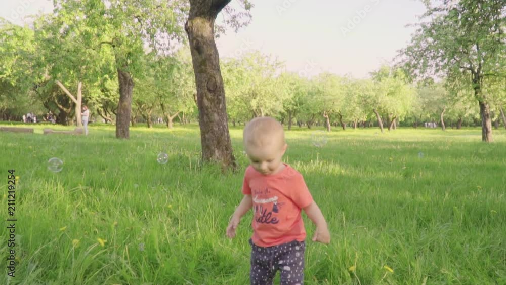 little boy looks at soap bubbles in park by parents hand. slow-mo