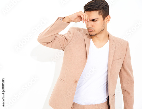 portrait of handsome fashion stylish hipster lumbersexual businessman model dressed in elegant light pink suit posing near white wall in studio. Metrosexual