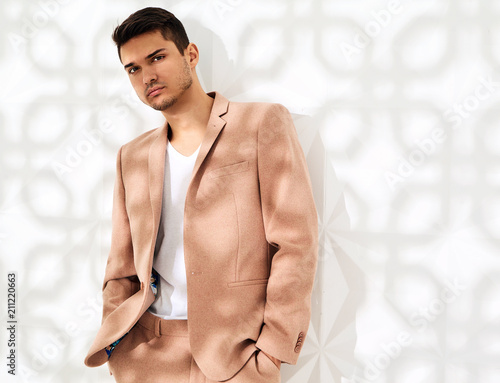 Fashion stylish lumbersexual model dressed in elegant light pink suit posing near white wall in studio. Metrosexual