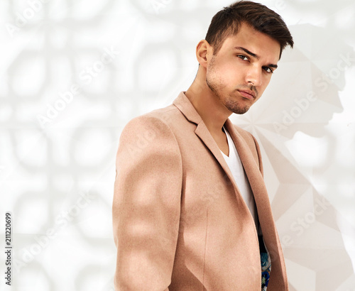 Fashion stylish lumbersexual model dressed in elegant light pink suit posing near white wall in studio. Metrosexual