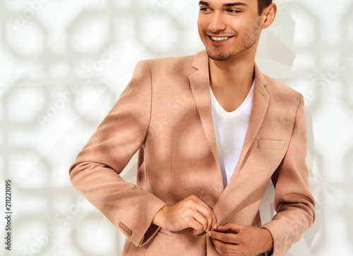 Fashion stylish lumbersexual model dressed in elegant light pink suit posing near white wall in studio. Metrosexual
