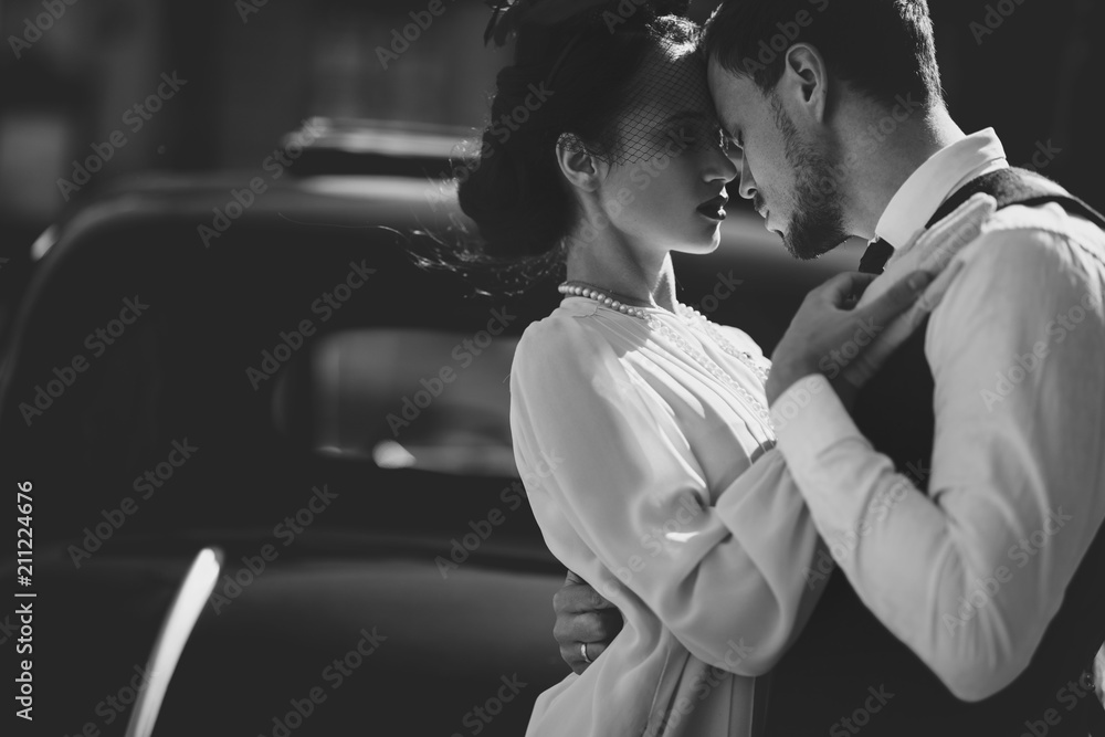 Lovely couple dressed in 30's style hugs on the street standing before an old car Lovely couple dressed in 30's style hugs on the street standing before an old car