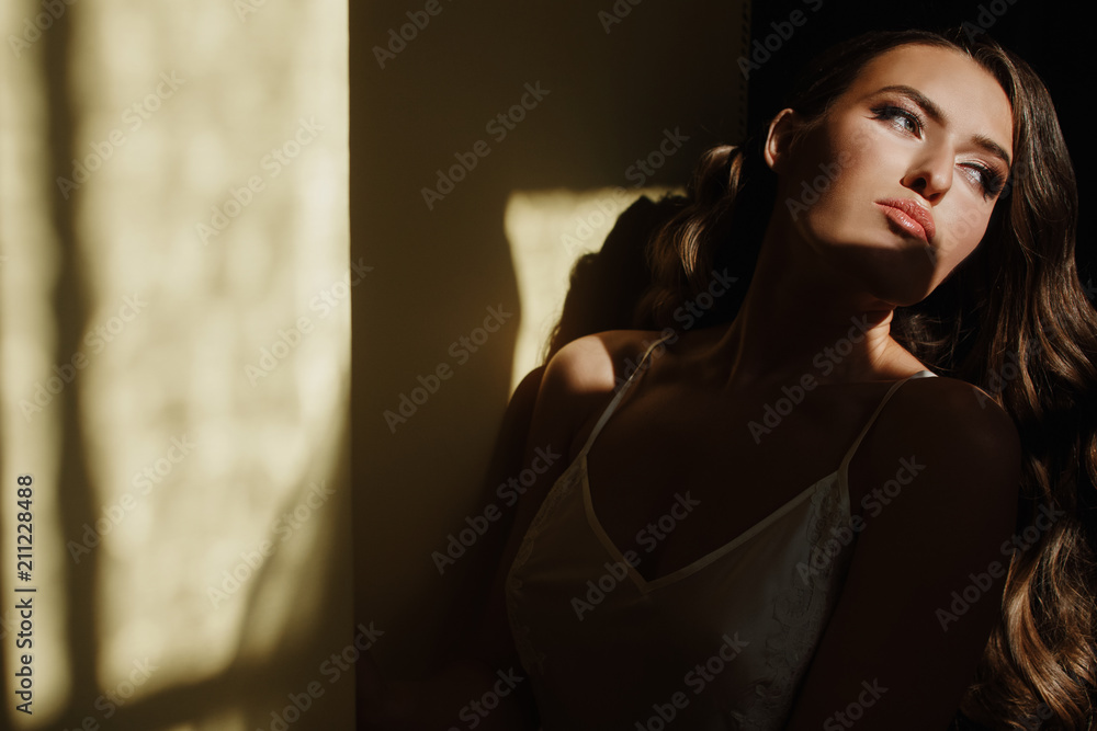 Seductive young bride in a silk dress sits on the windowsill in the early morning Seductive young bride in a silk dress sits on the windowsill in the early morning