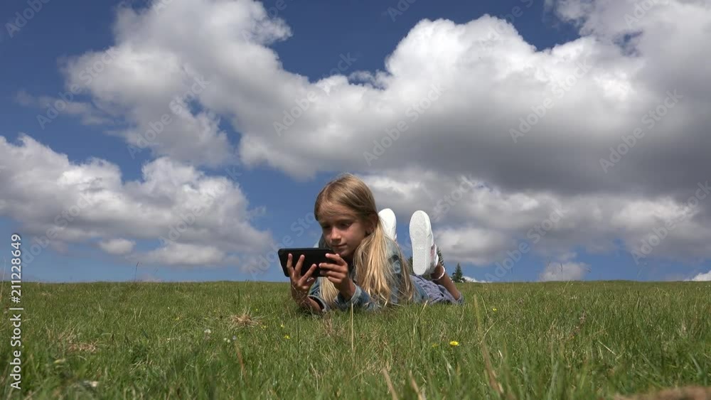 Child Playing Tablet Outdoor in Park, Kid use Smartphone on Meadow Girl in Grass Child Playing Tablet Outdoor in Park, Kid use Smartphone on Meadow Girl in Grass