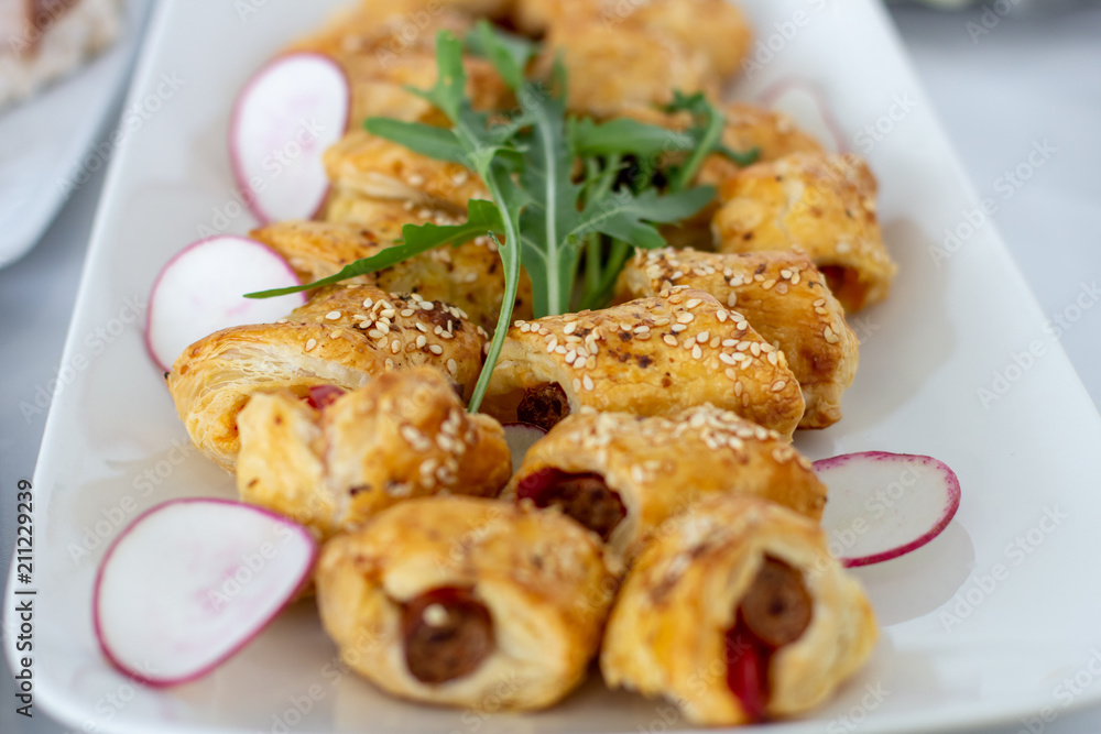 Snacks from puff pastry with sausage in the middle, sprinkled with sesame, decorated with arugula and radish Snacks from puff pastry with sausage in the middle, sprinkled with sesame, decorated with arugula and radish