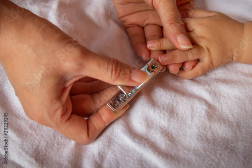 Mother's hand is using nail scissors to cut the nail to baby. Selective focus.