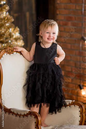 Little girl in black dress sits among Christmas decorations