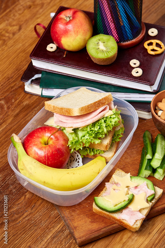 Foto Concept of school lunch break with healthy lunch box and school supplies on wooden desk, selective focus