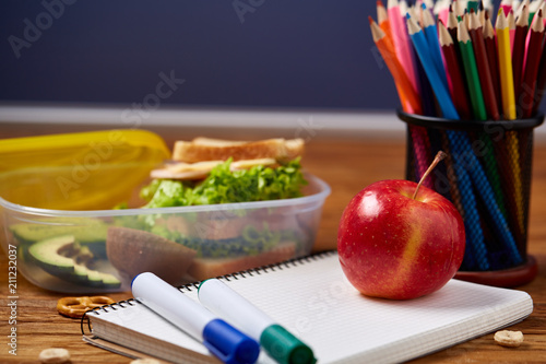 Concept of school lunch break with healthy lunch box and school supplies on wooden desk, selective focus.