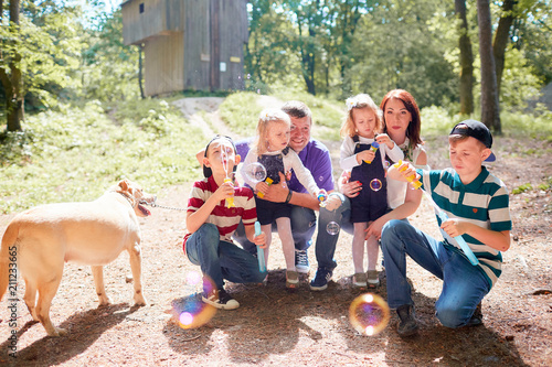 The children blowing bubbles and mother,father and  dog sitting near them