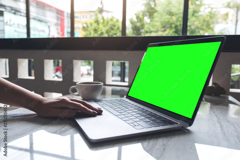 Mockup image of a woman using and typing on laptop with blank screen and coffee cup on table in modern cafe Mockup image of a woman using and typing on laptop with blank screen and coffee cup on table in modern cafe