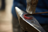 Close-up of a blacksmith's hands manipulating a metal piece above his forge, selective focus.