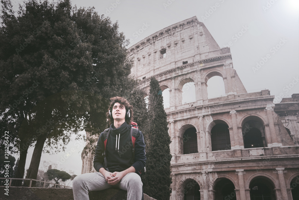 Handsome young man with headphones listening to music in front of Colosseum in Rome
