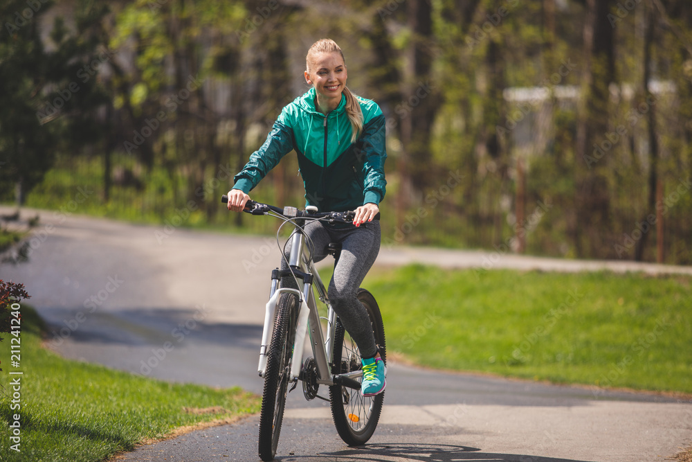 Young pretty lady is riding bike in park and smiling. She is enjoying sunny weather and environment around her. Copy space in right side
