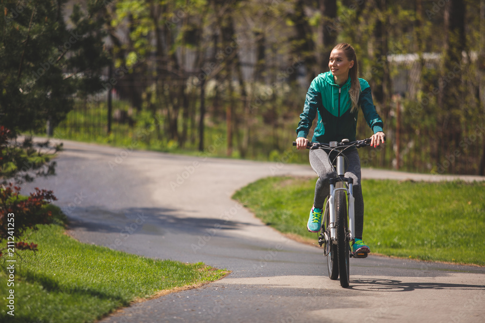 Happy calm lady is riding bike along path outdoors. She is looking at nice green nature around her. Copy space in left side Happy calm lady is riding bike along path outdoors. She is looking at nice green nature around her. Copy space in left side
