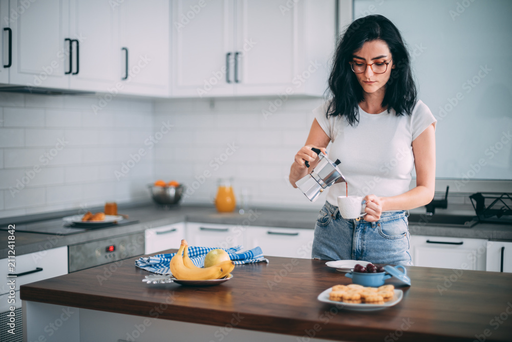 Beautiful young woman pouring coffee in the kitchen Beautiful young woman pouring coffee in the kitchen
