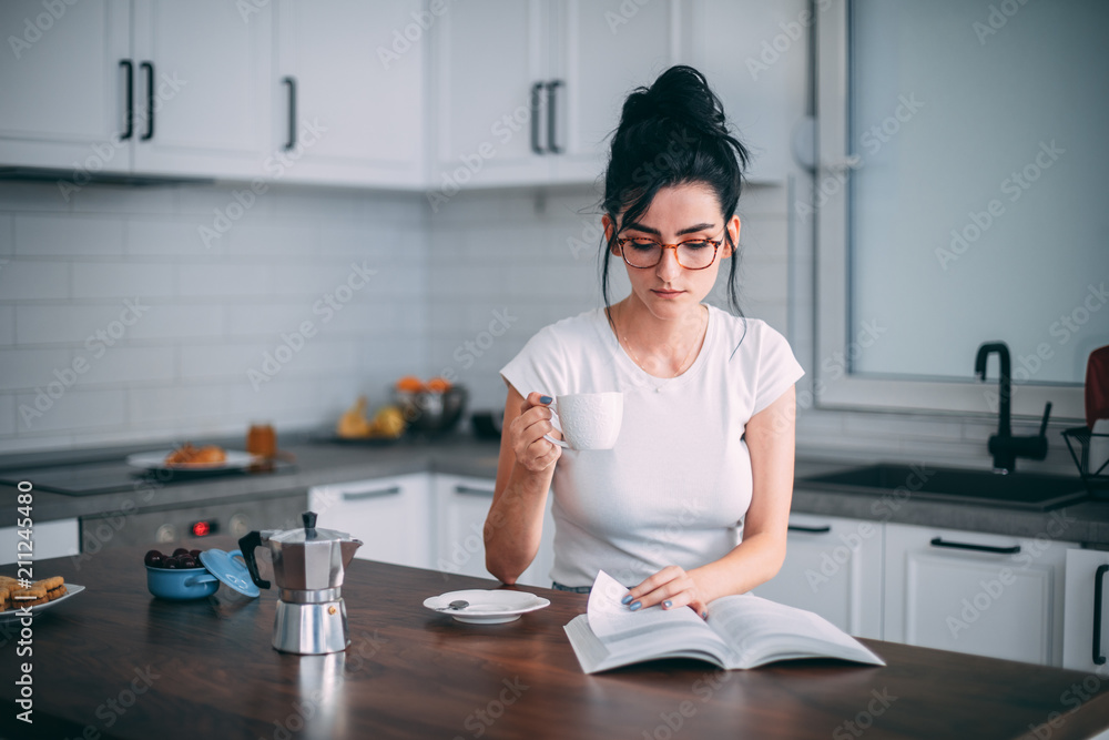 Beautiful young woman reading book in the kitchen