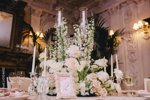 Decorated elegant banquet table in a classic style in the mansion. Decorated with bouquets of white flowers from roses and buttercups, glass candlesticks, cutlery and candles