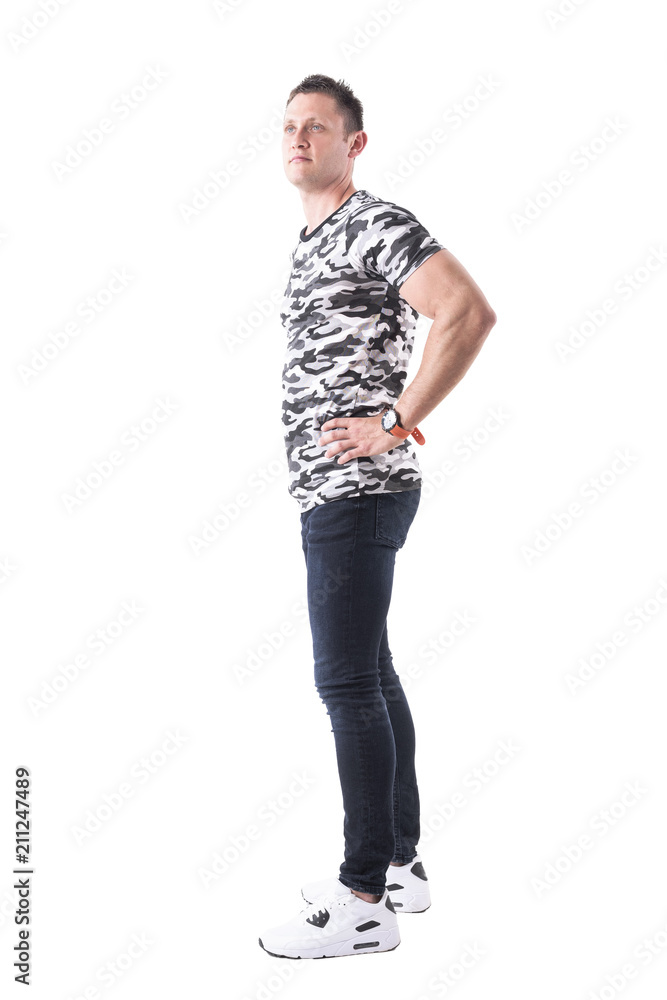 Profile of confident sport casual man in military shirt with hands on hips looking up. Full body isolated on white background. 