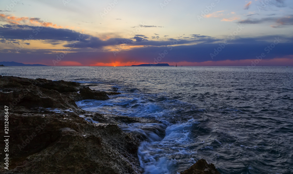 Cluodly sunset with setting sun among storm clouds at sea off the coast of volcanic rock, Crete, Greece