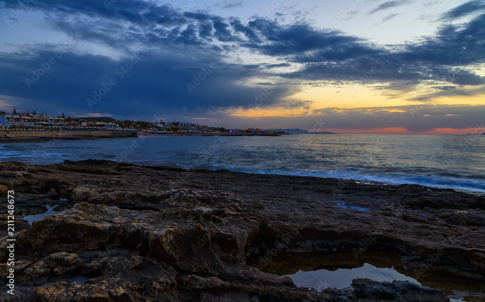 Seascape. Sun in the clouds at sunset over the sea and resort town on the island of Crete