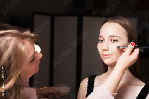 makeup artist dabbing the mixed foundation on a face skin of a young beautiful model girl. concept of professional make up training