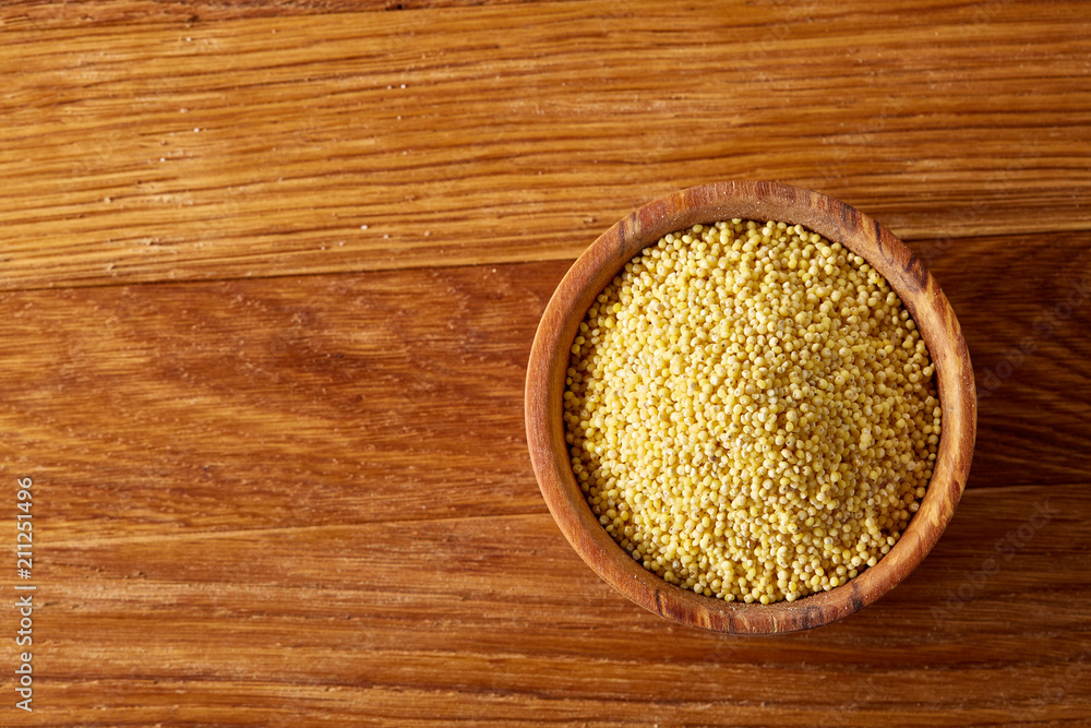 A wooden dish with millet on rustic wooden background, top view, close-up, selective focus. A wooden dish with millet on rustic wooden background, top view, close-up, selective focus.
