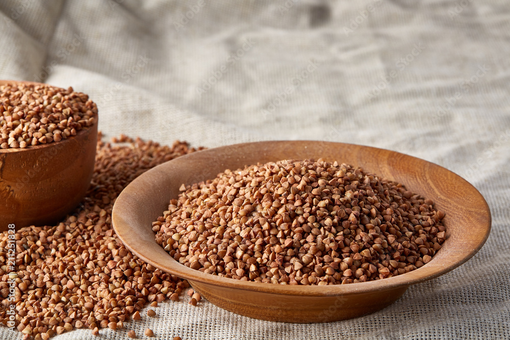 Bowl and plate full of buckwheat grains on homespun tablecloth, close-up, selective focus, shallow depth of field. Bowl and plate full of buckwheat grains on homespun tablecloth, close-up, selective focus, shallow depth of field.