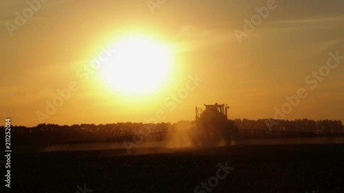 Tractor spraying chemicals in a field at sunset. Fertilizer application in the field of corn at sunset of the day.
