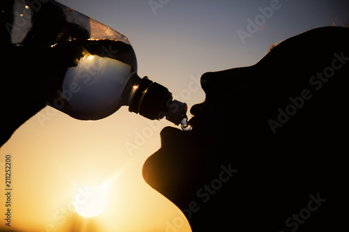 Silhouette of a woman drinking water at sunset photo
