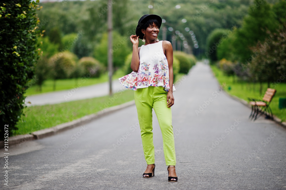 Amazing african american model woman in green pants and black hat posed with different emotions at park.