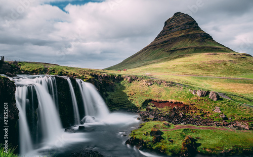 sun covered kirkjufellsfoss waterfall with kirkjufell mountain in iceland. picturesque long exposure of famous iceland nature