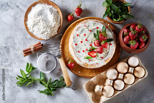 Strawberry tart covered with whipped sour cream surrounded by organic ingredients over white background, flat lay. photo